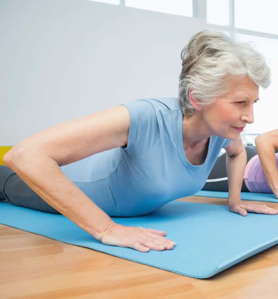 пожилая женщина с болями в спине делает упражнения на растяжку по методу Маккензи