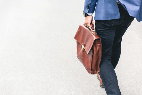 A person walking holding a brown leather bag.